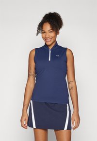 Top sem mangas azul marinho com gola com fecho e logo CK, combinado com uma saia correspondente com listas brancas laterais. Textura de tecido suave.