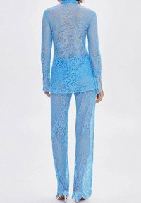 Lichtblauw kanten pak met een doorschijnende top met lange mouwen en wijde broek met een bloemenpatroon en franjes aan de zomen.