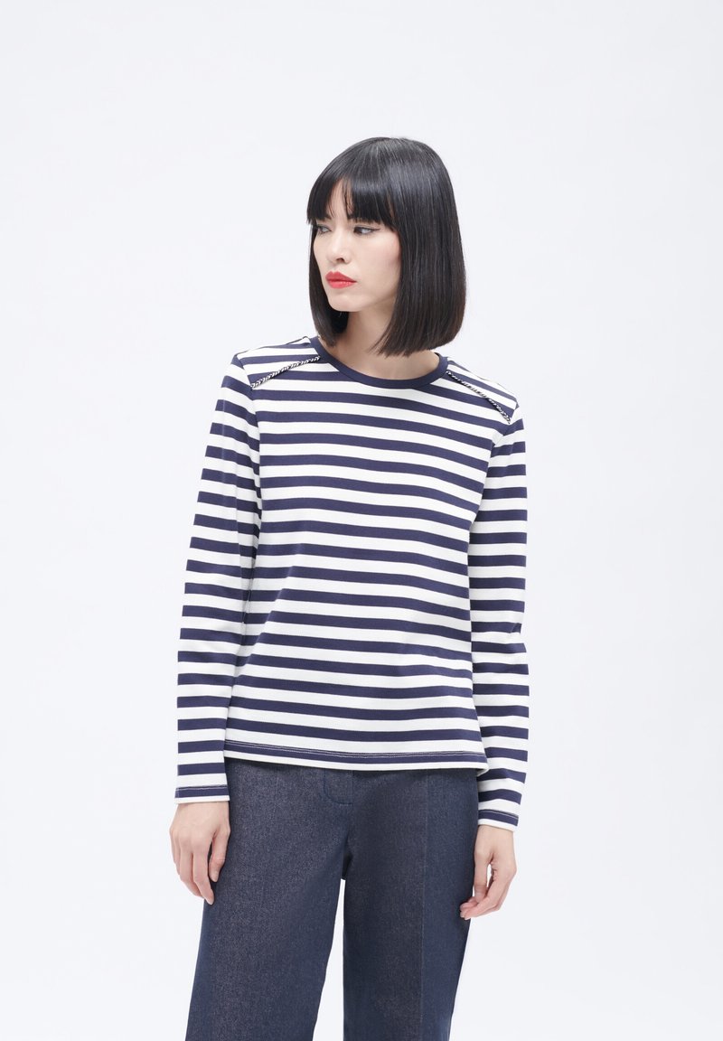 Marineblauw en witte gestreepte langemouwen shirt met een ronde halslijn, met accenten op de schouders. Combinatie met donkerblauwe wijde broek.