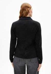 Blazer nero con una vestibilità su misura, collo a risvolto e maniche lunghe. Tessuto morbido con un design semplice, abbinato a jeans grigi.