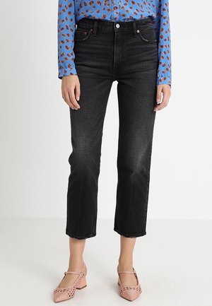 Sorte højtaljede jeans med lige ben, der har en knaplukning og fem lommer, kombineret med en blå mønstret bluse og lyserøde sko.