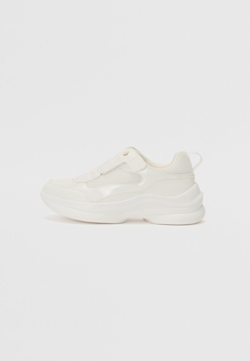 Des chaussures de sport blanches avec une tige en synthétique lisse, des accents en maille, une semelle rembourrée et un design texturé avec une languette à l'arrière.