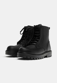 Bottes montantes en cuir noir avec bouts arrondis, coutures renforcées et semelles en caoutchouc à crampons. Caractéristiques : laçage à l'avant et texture solide et lisse.