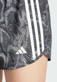 Mustavalkoiset urheilushortsit, joissa on käärmeennahkakuosi. Sivulla kolme valkoista raitaa ja valkoinen logo helmassa.