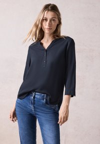 Marineblouse met een henley-halslijn, driekwartmouwen en knopen. Gecombineerd met blauwe spijkerbroeken, lijkt de stof zacht en glad.