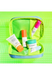 Compact green skincare bag with mesh interior, containing various bottles and jars in vibrant colors: orange, pink, white, and teal.