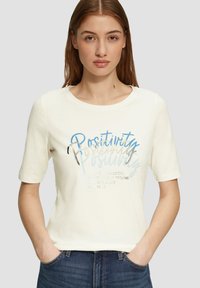 Crème korte mouwen t-shirt met een ronde halslijn, voorzien van blauwe en metallic zilveren tekst met de woorden "Positiviteit" en motiverende zinnen.