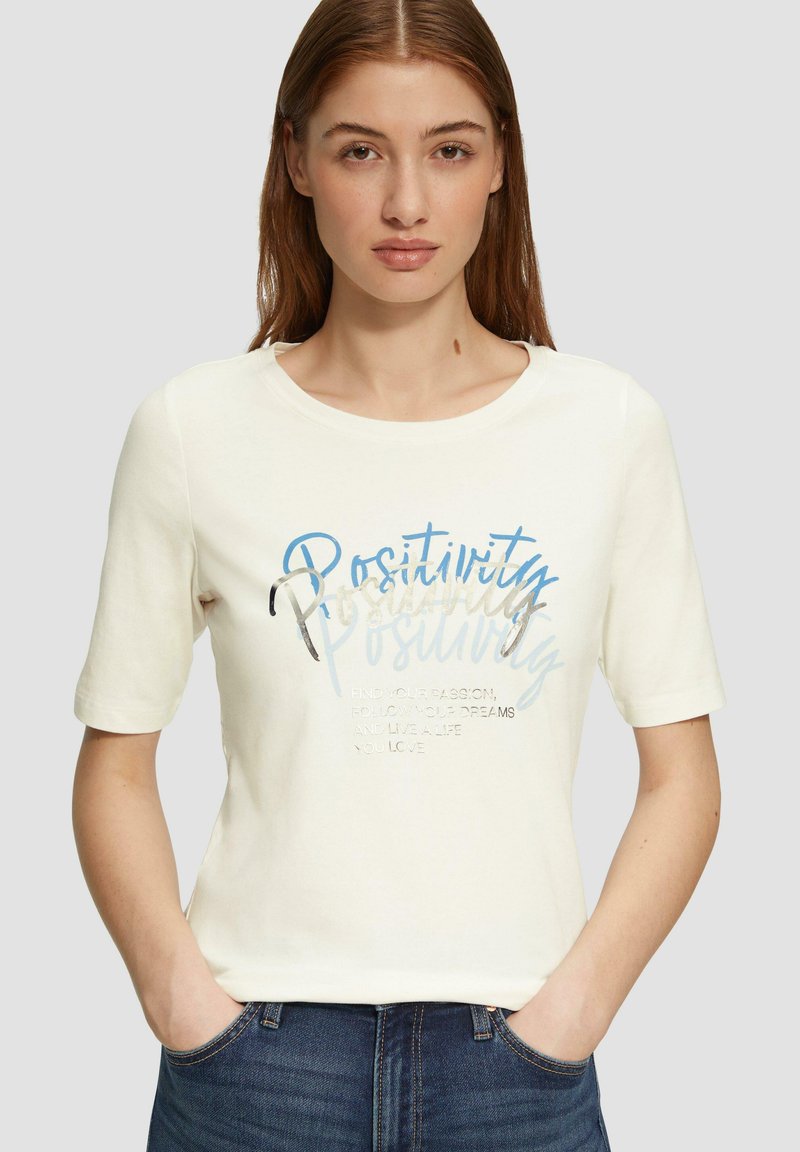 Crème korte mouwen t-shirt met een ronde halslijn, voorzien van blauwe en metallic zilveren tekst met de woorden "Positiviteit" en motiverende zinnen.