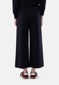 Weite marineblaue Hosen aus glattem Stoff, mit einem hoch sitzenden Design, kombiniert mit burgunderfarbenen Sneakern mit weißen Akzenten.