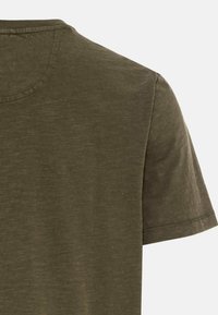 T-shirt manches courtes vert olive avec col rond et coutures apparentes sur les bordures des épaules et des manches, sur un fond uni.