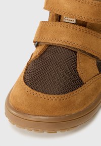 Bruine suède schoen met gaaspanelen en dubbele klittenbandsluitingen. Ronde neus en getextureerde rubberen zool. Geweven details overal.