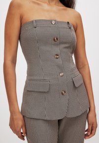 Hnedý a krémový károvaný bezramienkový top s piatimi gombíkmi, prispôsobený strih a dve predné vrecká. Textilná látka s jemným vzorom.