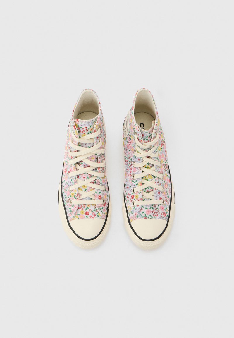 Hoch geschnittene Segeltuch-Sneaker mit weißen Gummikappen an den Zehen und Sohlen, bedeckt mit einem bunten kleinen Blumendruck, von oben vor weißem Hintergrund gezeigt.