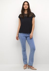 Black top with lace detail on shoulders, paired with light blue jeans. The top features a round neckline and short sleeves. Light beige shoes.