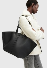 Grand tote en cuir noir avec deux poignées solides, arborant une conception angulaire et structurée ainsi qu'une texture lisse.