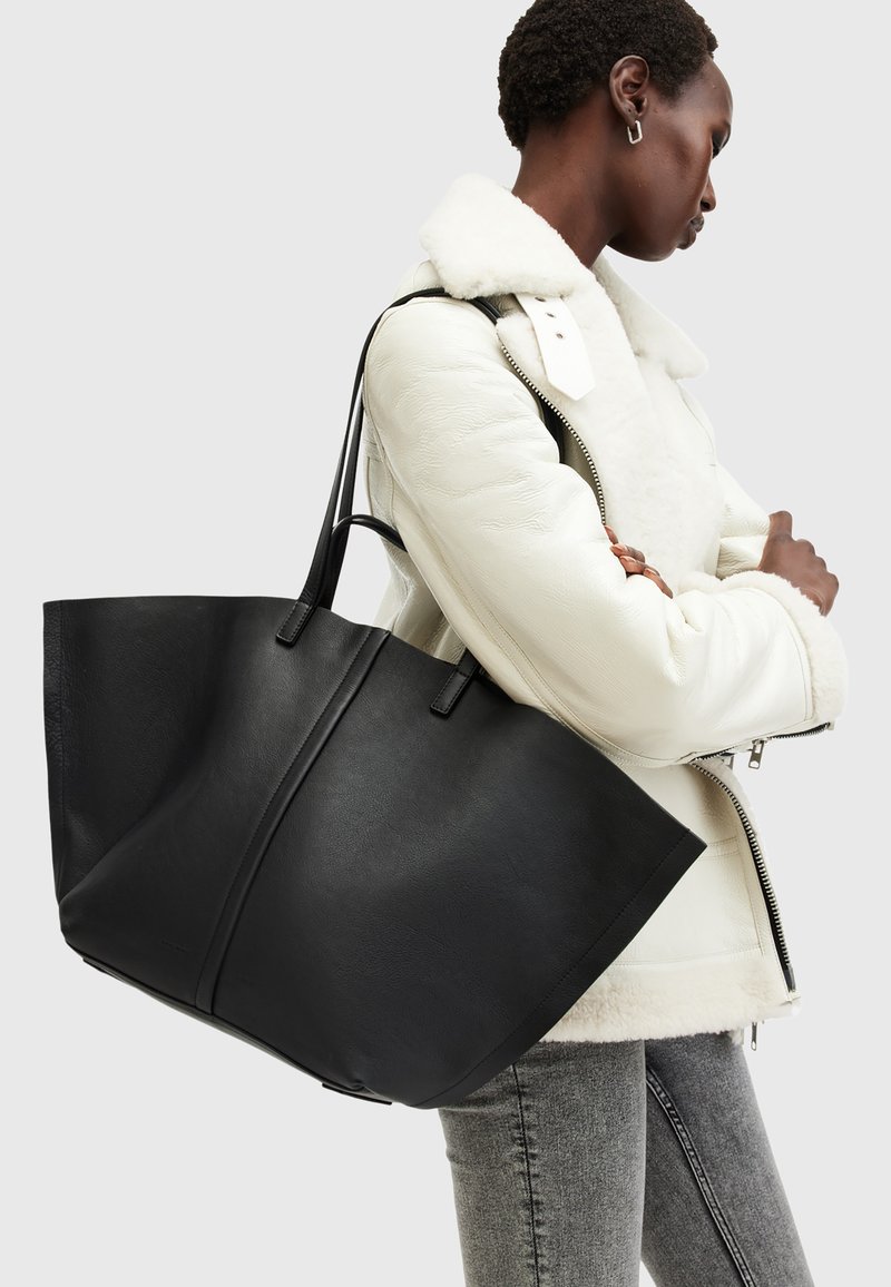 Grand tote en cuir noir avec deux poignées solides, arborant une conception angulaire et structurée ainsi qu'une texture lisse.