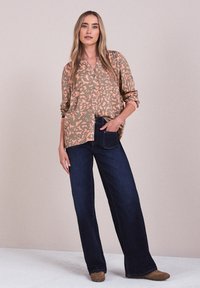 Blouse à motif floral dans des tons beige doux et corail, associée à un jean large bleu foncé. Tissu doux avec fermeture à boutons et manches retroussées.
