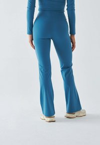 Dzwoniaste spodnie sportowe w jednolitym kolorze teal, wykonane z elastycznej tkaniny, z wysokim paskiem i gładkim, dopasowanym krojem.