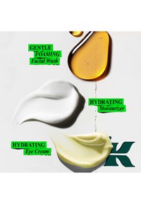 Gouttes de liquide ambré, crème blanche et crème jaune avec étiquettes nettoyant visage moussant doux, hydratant visage et crème hydratante pour les yeux sur une surface blanche.