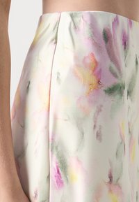 Jupe fleurie en tissu léger présentant des teintes pastel de rose, jaune et vert, avec une texture douce et des plis latéraux.