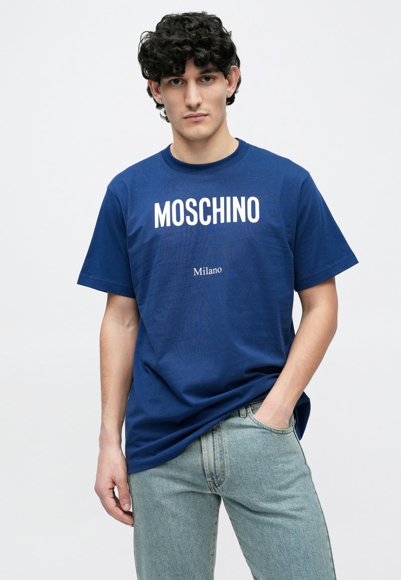 Donkerblauw katoenen T-shirt met "MOSCHINO"-opdruk in het wit, korte mouwen en een afgeronde halslijn. Gecombineerd met lichtblauwe spijkerbroek.