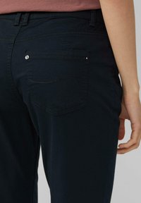 Dunkelnavy Hosen mit einer glatten Textur, fünf Taschen-Design und dekorativen Nähten auf den Gesäßtaschen. Subtile metallische Hardware-Akzente.