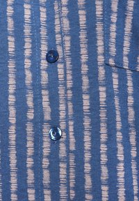 Plava lanena košulja s vertikalnim krem prugama, džepom na patchu i plavim dugmadi. Mekana tekstura s opuštenim uzorkom.