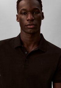 Juoda polo marškinėliai su apykakle ir trimis mygtukais, su mažu logotipu ant krūtinės. Lygus tekstūra ir aptakus dizainas.