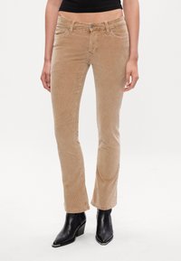 Beige corduroy broek met een slim fit en uitlopende onderkant, voorzien van een sluiting met een voorknoop en twee voorzakken, gedragen met zwarte enkellaarsjes.