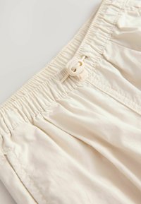 Lys beige shorts med en samlet elastisk talje med en trækflap, lavet af blødt, struktureret materiale; inkluderer subtile syninger.