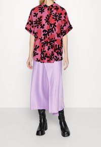 Camicia a maniche corte rosa con motivi floreali neri, abbinata a una gonna lavanda fluida e stivali neri fino al ginocchio.