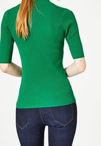 Zelený pruhovaný top s přiléhavým střihem a krátkými rukávy, kombinovaný s tmavě modrými džíny, které mají hladkou texturu a jemné detaily šití.