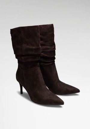 Paire de bottines en daim marron foncé avec des tiges souples et pliées, bouts pointus et talons hauts et fins.