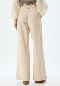 Beige wijde pijpenbroek van katoen, met een hoge taille, twee achterknopen en een gladde, gelijkmatige textuur.