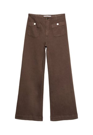 Pantalones marrones de talle alto con bolsillos delanteros de parche y botones de latón, combinados con un suéter blanco tejido de canalé corto y una pulsera de cuero con tachuelas.