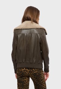 Brun läderjacka med en beige fårskinnskrage, ribbade muddar och midja. Baksidan har synliga sömmar och en jämn textur.