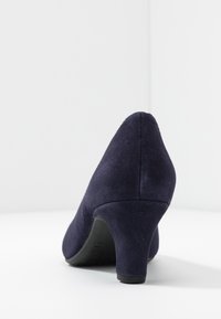 Chaussure à talon haut en daim bleu marine avec un bout pointu et un talon rond. Texture lisse avec une finition mate, sans motifs ni accents visibles.