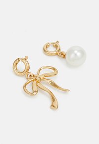 Goldene Creolen mit einem Schleifen-Design und einem weißen Perlenakzent. verfügen über glänzende, glatte Oberflächen und filigrane Details.