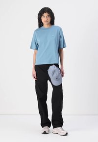 Lys blå kortermet T-skjorte, svarte løstsittende bukser, grå caps balansert på buksene, og grå joggesko. Glatt stoff, avslappet design.