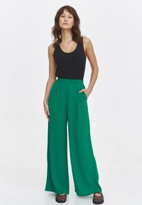 Zielone spodnie o szerokich nogawkach z elastycznym pasem i kieszeniami po bokach, w zestawieniu z dopasowaną czarną bluzką na ramiączkach. Gładki materiał, casualowy design.