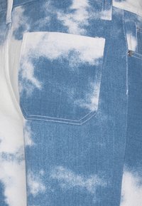 Blå och vit tie-dye denimtyg med en bakficka med kraftig söm och texturerad finish. Molnliknande mönster över materialet.