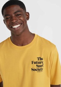 Dzeltena kokvilnas T-kreklu ar melnu uzdrukātu tekstu "The Future Surf Society" un "O'Neill" kreisajā krūšu daļā. Īsās piedurknes un apaļa kakla izgriezums.