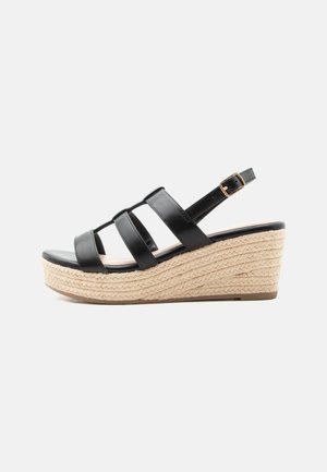 Černá kožená wedge sandála s nastavitelnou kotníkovou přezkou a proplétanou platformou z přírodní juty na bílém pozadí.
