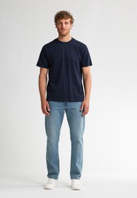 Marineblauw T-shirt met korte mouwen van zacht materiaal, gecombineerd met lichtblauwe jeans met rechte pijpen en witte sneakers. Simpel ontwerp en pasvorm.