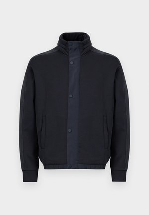 Donkerblauwe jas van zacht stof, met een hoge kraag, drukknoopsluiting, zijzakken en elastische manchetten en zoom.