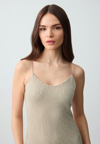 Gebreide jurk in lichtbeige met een zigzagpatroon, voorzien van dunne spaghettibandjes en een ronde hals. Glad textuur en aansluitende vorm.