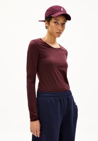 Langärmliges, weinrotfarbenes Oberteil aus weichem Stoff, kombiniert mit dunkelblauen Jogginghosen mit elastischem Bund. Accessoires umfassen eine passende Mütze.