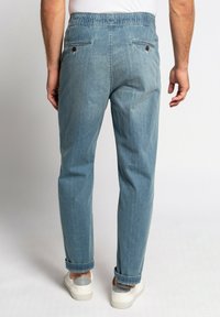 Pantalones de mezclilla azul claro con un ajuste relajado, que presentan una cintura elástica, dos bolsillos traseros y puños doblados. Tejido texturizado con un acabado sutil.