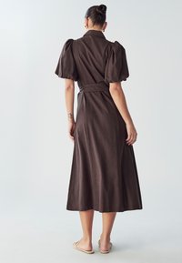 Hnědé midi šaty s krátkými nabíranými rukávy, páskem v pase a měkkou tkaninou. Mají límeček a sahají až k polovině lýtek.