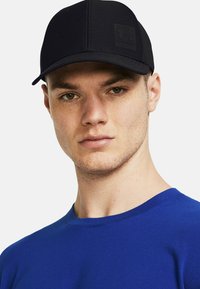 Sort struktureret kasket med flad skygge og logo-patch, parret med en blå crew neck t-shirt. Glat stof og rene linjer er fremtrædende.